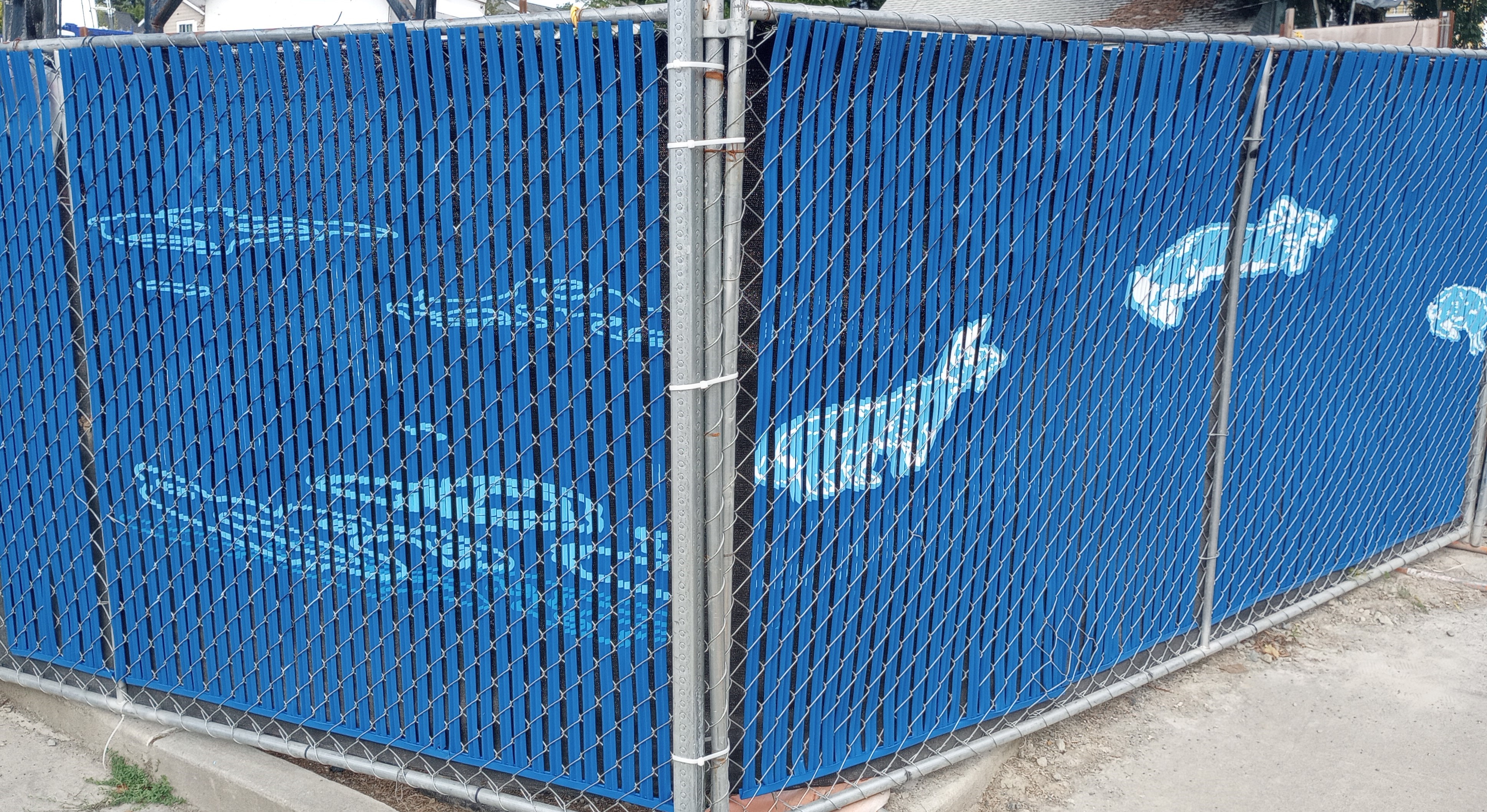  Blue inserts woven into a chainmail fence, with a mural of clouds painted on one side and an illustration of a corgi in mid-jump on the other.