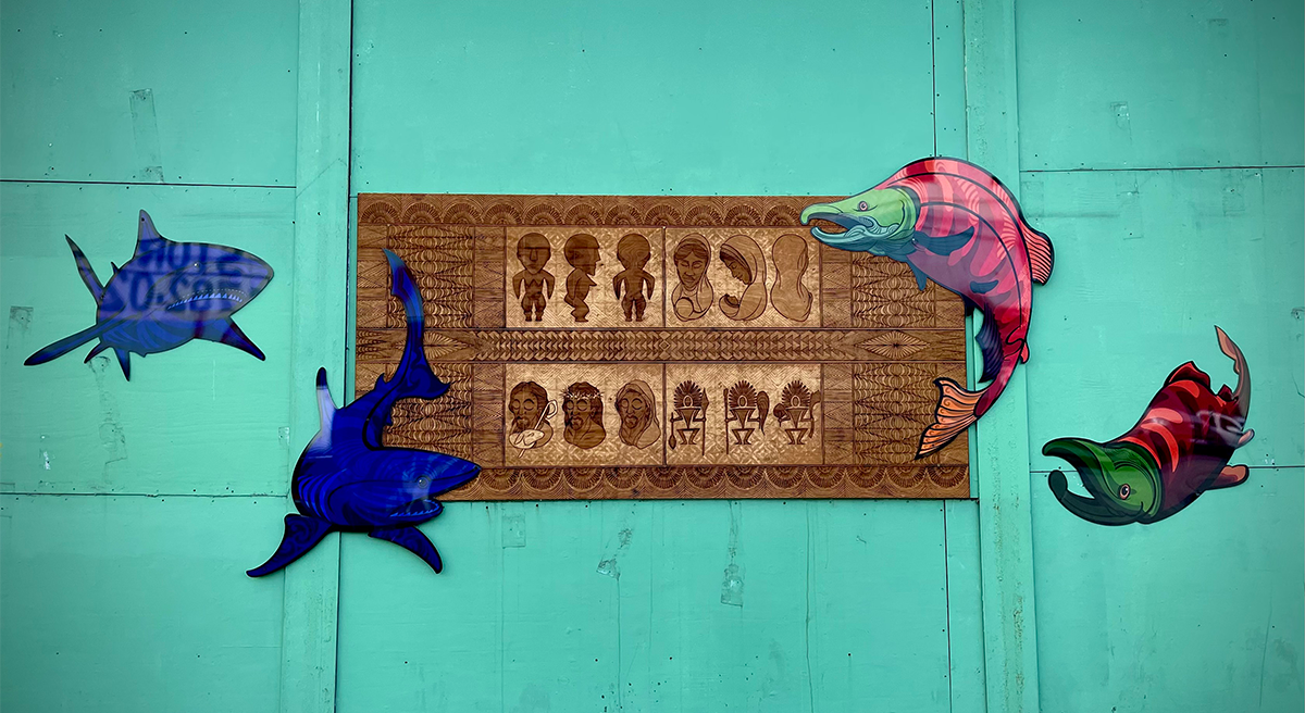 This photo shows drawings of sharks and salmon that appear to be swimming around a native wood carving.