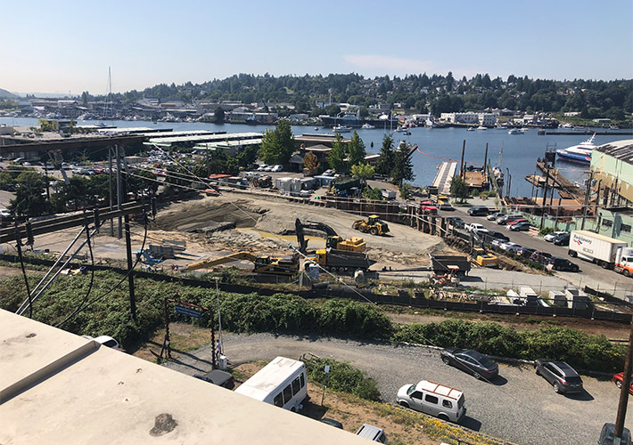 Excavators and construction crews prepare the future Ballard construction site at Shilshole Avenue Northwest and 24th Avenue Northwest on a sunny day.